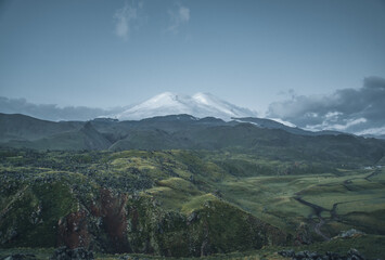 Natural landscape with a hilly valley and Mount Elbrus in the center of the frame.
