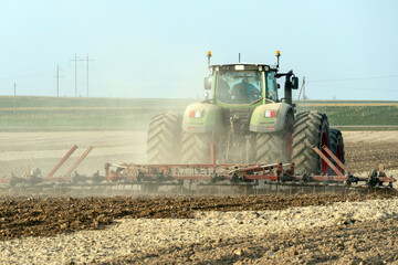 agricultural machinery works in the field. A tractor with a plow and a cultivator cultivates the land before sowing wheat and other cereals. The farmer plows the land very nicely and carefully.