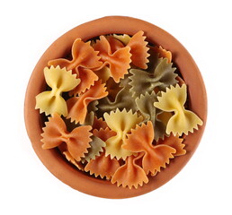 Pasta farfalle tricolore pile made from durum wheat in clay pot isolated on white background, top view