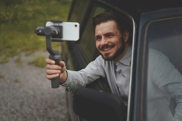 Portrait of millennial man recording video at smartphone with steadycam