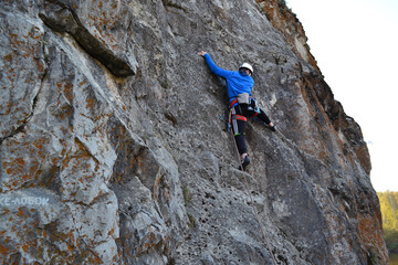 A rock climber in a white helmet climbs a rock in evening