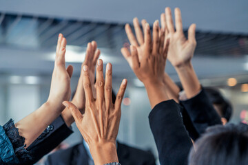 Many happy business people raise hands together with joy and success. Company employee celebrate after finishing successful work project. Corporate partnership and achievement concept.