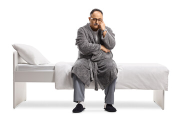 Pensive mature man in pajamas and a robe sitting on a bed