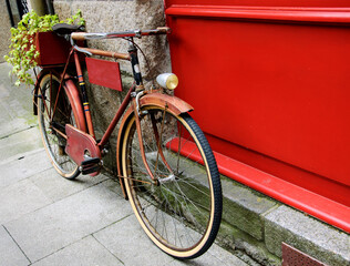 Fototapeta na wymiar Rusty vintage red bicycle leaning with on red wooden board (useful for entering a text advertisement, menu etc) and carrying plants in wooden box as decoration.