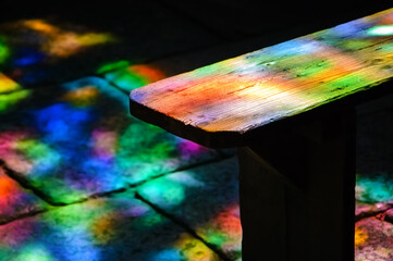 Colorful light spots on the wooden bench and stone floor in church. Sunlight filtered through the...