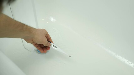 Closeup footage of man's hand using thermometer to check water temperature in bath. Man is preparing a hot water to taking a bath. He wants to relax after busy day. Bath for baby.