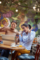 Two cheerful female students are joking while have a chat on a laptop in bar's garden. Leisure, bar, friendship, outdoor