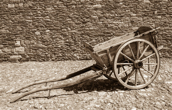 Old wooden carriage on the pavement and rough stone wall at background. Sepia historic photo.