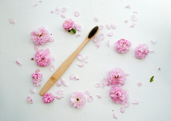 A bamboo toothbrush on a white background surrounded by pink flowers.