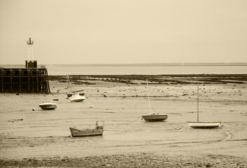 Sailing and fishing boats lying on sea floor at low tide and a lighthouse at small harbor near Saint-Malo in the dusk . Brittany, France. Business on the rocks /  in low water metaphor. Sepia photo