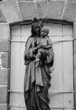 Statue of Madonna with Child in front of the window (closed with shutter). Brittany, France. Protection and security concepts. Black white historic photo. 