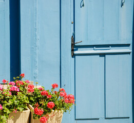 A wooden house door and geranium flowers in the boxes in sunny day. Brittany, France.
