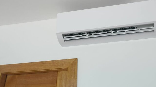 Flat air conditioner on white wall in room interior. Man pushing button on remote. Setting temperature
