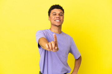 Young African American man isolated on yellow background showing and lifting a finger