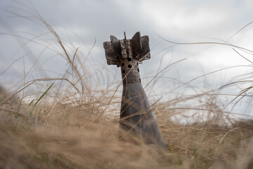 An unexploded rusty mortar mine poses a hazard in withered grass on a cloudy spring day