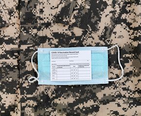 Covid 19 vaccination record card and personal facemask on military uniform