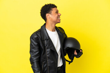 Young African American man with a motorcycle helmet isolated on yellow background laughing in lateral position