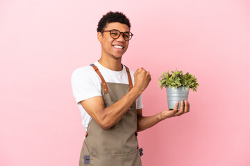 Gardener African man holding a plant isolated on pink background celebrating a victory