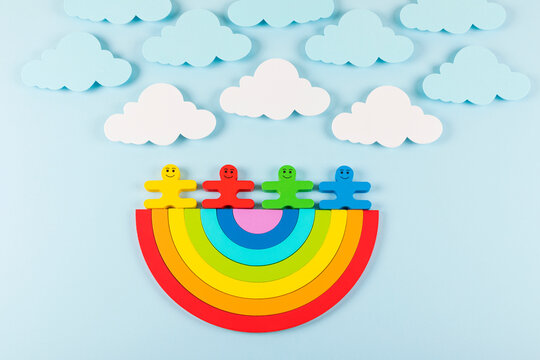 International Children's Day background. Wooden toy children with the rainbow on the light blue background. Flat lay. Copy space.