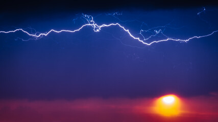 Amazing Lightning at Sunset. Thunderstorm horizontal lightning discharge in the dark sky above the orange sun. Lightnings in red Stormy sky. Dramatic moody cloudspace.