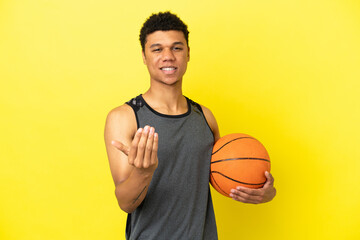 African American man isolated on yellow background playing basketball and doing coming gesture