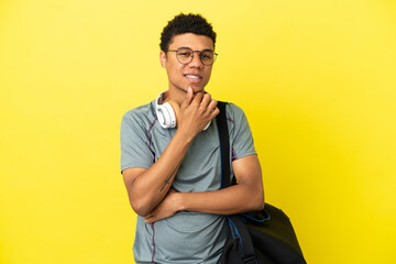 Young sport African American man with sport bag isolated on yellow background with glasses and smiling