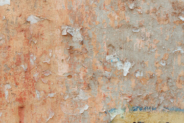 A red-yellow fragment of a concrete wall with a copious amount of scratches. Rough surface with scuffs and cracks. Remains of announcements: glue and paper.