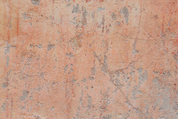 A red-yellow fragment of a concrete wall with a copious amount of scratches. Rough surface with scuffs and cracks.