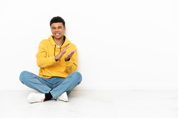 Young African American man sitting on the floor isolated on white background applauding after presentation in a conference