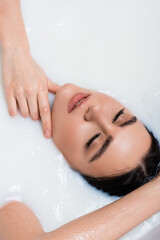 Naklejka premium overhead view of woman with closed eyes touching neck while taking milk bath.