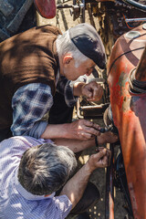 Two caucasian senior men father and son pensioner at the farm repairing the tractor machine in sunny day family bonding generation cooperation and togetherness concept real people