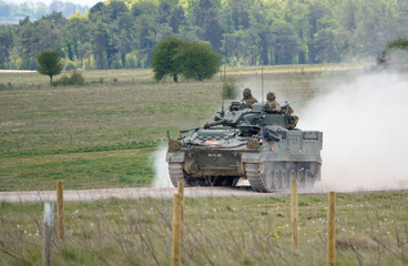 British Army Warrior FV510 Light Infantry Fighting Vehicle travelling at high speed and kicking up clouds of dust, on maneuvers Salisbury Plain military training grounds, Wiltshire