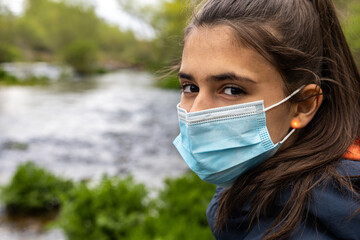 Portrait of a happy young teenage girl with a mask by a stream or river in Covid19 time with selective focus