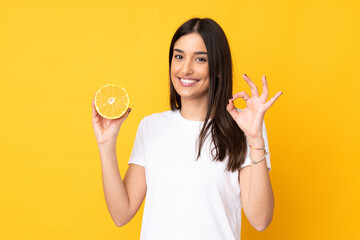 Young caucasian woman holding an orange isolated on yellow background showing ok sign with fingers