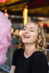 Chica rubia guapa con algodón de azucar rosa sonriendo en zona de atracciones de una feria