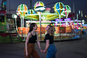 Dos chicas pasándolo bien abrazándose en zona de atracciones de una feria