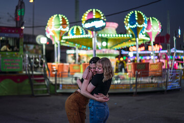 Dos chicas pasándolo bien abrazándose en zona de atracciones de una feria