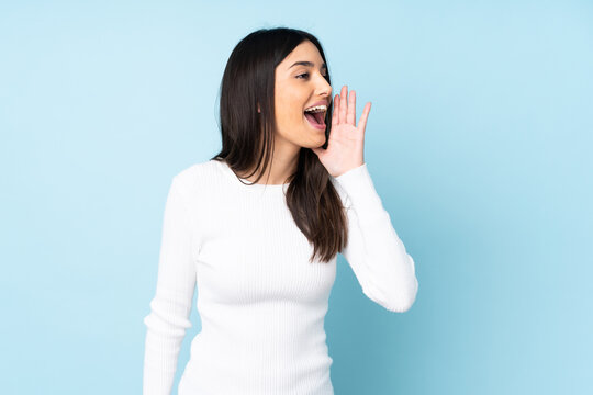 Young caucasian woman isolated on blue background shouting with mouth wide open to the side