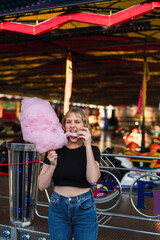 Chica rubia guapa comiendo algodón de azúcar en zona de atracciones de una feria