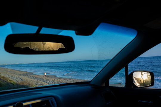 A couple embrace romantically on a California beach seen from a car interior