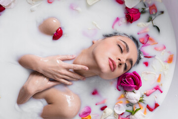 Fototapeta na wymiar seductive woman touching neck while taking milk bath with rose petals.