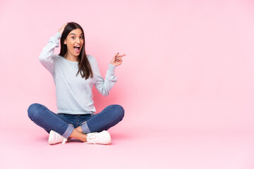 Young caucasian woman isolated on pink background surprised and pointing finger to the side