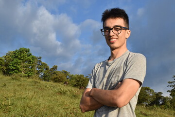 HOMBRE JOVEN DE GAFAS EN LA MONTAÑA EN DIA SOLEADO SONRIENTE