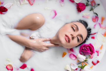 Obraz na płótnie Canvas sensual woman touching neck while taking milk bath with rose petals.