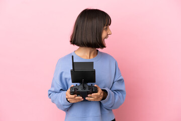 Young mixed race woman holding a drone remote control isolated on pink background laughing in lateral position