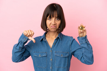 Young mixed race woman holding a Bitcoin isolated background showing thumb down with negative expression