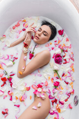 Plakat top view of pretty woman bathing in milk with rose petals.