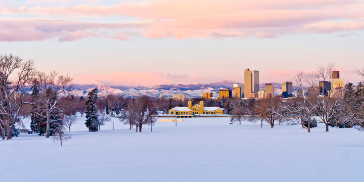 Downtown Denver Skyline from City Park at dawn on a cold January Morning with brightly lit pink and purple clouds over the foothills and the City Park Pavilion in the foreground with a snow covered pa