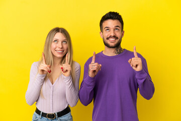 Young couple over isolated yellow background pointing up with the index finger a great idea