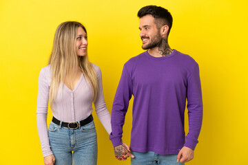 Fototapeta premium Young couple over isolated yellow background holding hands